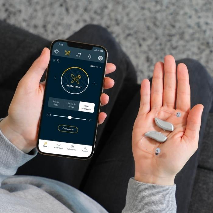 Hand holding Jabra Enhance hearing aids and using Jabra app